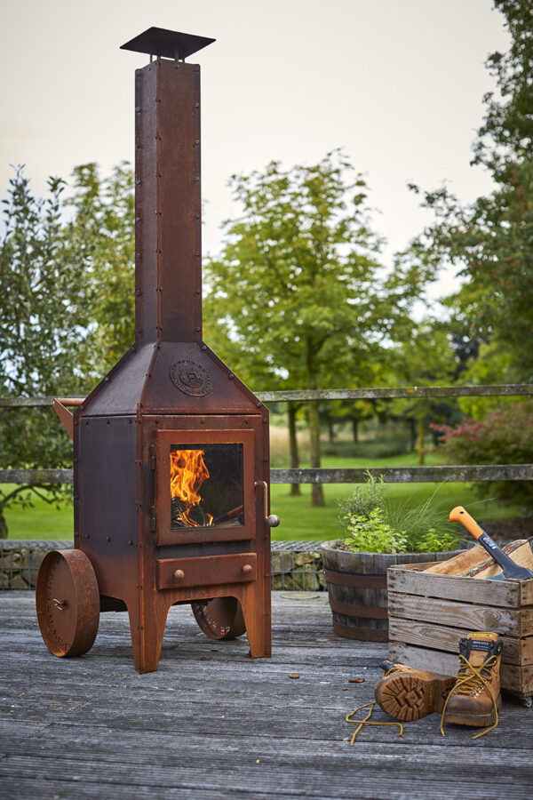 RB73 Bijuga - RB73 Bijuga The Bijuga is a robust CorTen steel outdoor stove. The striking timeless design combines tight lines and surfaces with industrial accents. The sheet material is folded out on the connecting seams and all bolts and nuts are visible. The hardwood merbau parts (knobs and push-bar) not only provide beautiful details but are also very practical for operation because they do not get too hot. The design is from Atelier Rene Knip. Rene has a distinctive view on stoves. The user and the function of the fireplace are central. His designs have a distinct design and are characterized by balanced proportions in size, a beautiful look and the use of high-quality materials and beautiful details. At the backside it has 4 extra air inlets, this air ends up in the airspoiler that is positioned at the inside just above the glass. It will create a natural air layer to keep the glass clean. The 2-wheel version with a push-bar on the rear can easily be moved. The emblem on the hood is a symbol for the collaboration with Atelier Rene Knip, the designer of this stove.  