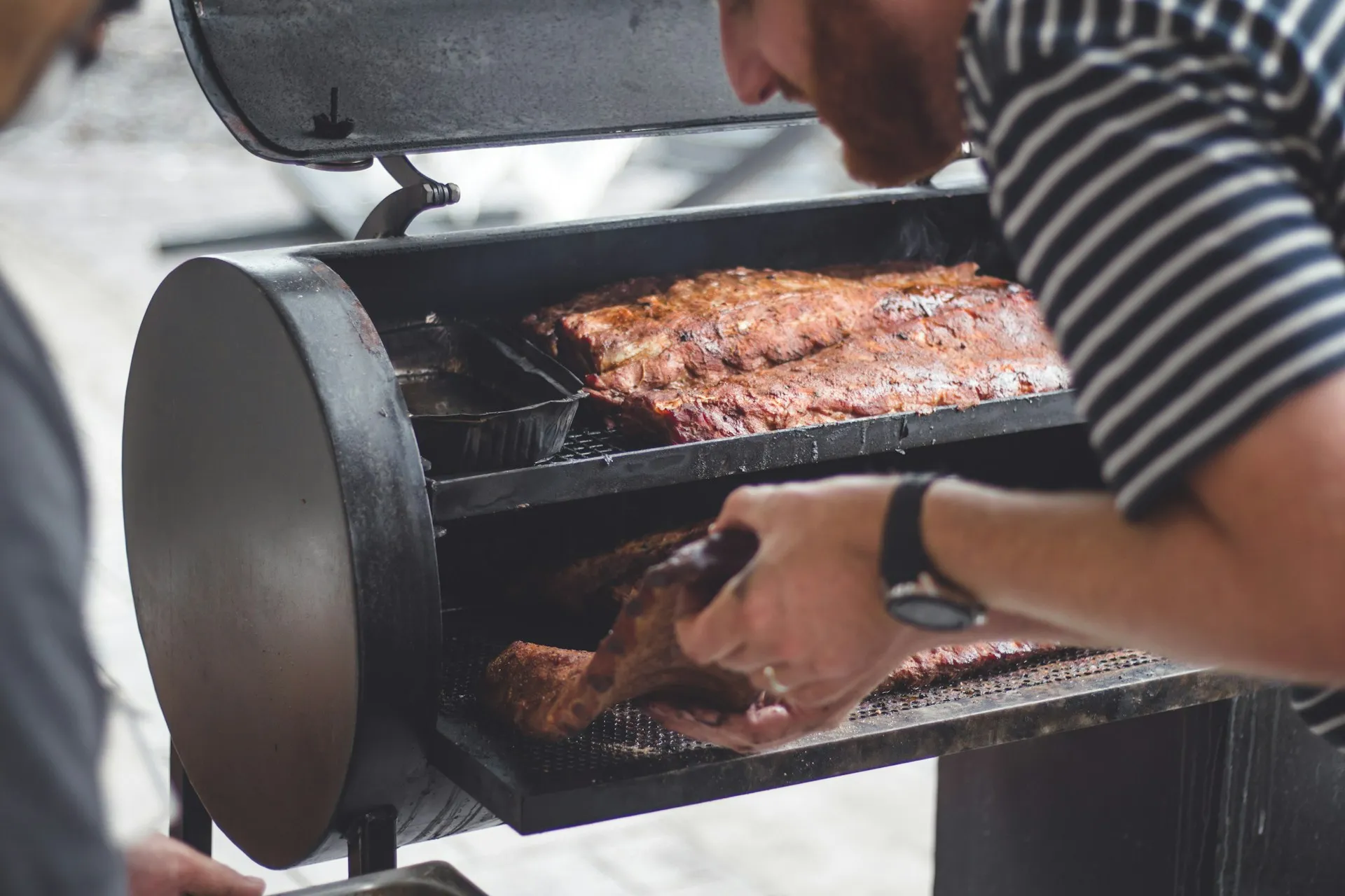 Person checking meat inside a smoker BBQ during a low-and-slow cook.