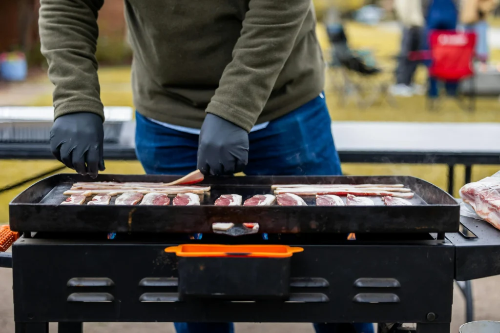 What Is a BBQ Plancha and Is It Worth It for UK Gardens? 1 Cook frying bacon outdoors on a flat-top BBQ plancha griddle.