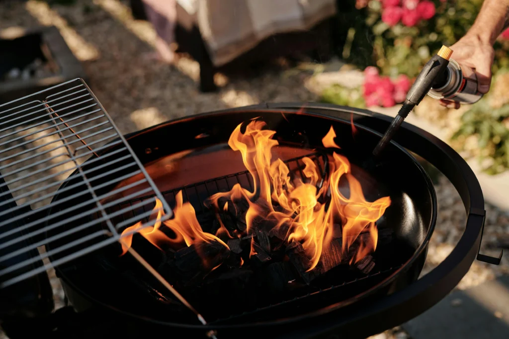 What Is a Wood-Fired BBQ and Is It Worth It? 2 Lighting a wood-fired charcoal kettle BBQ in a back garden.